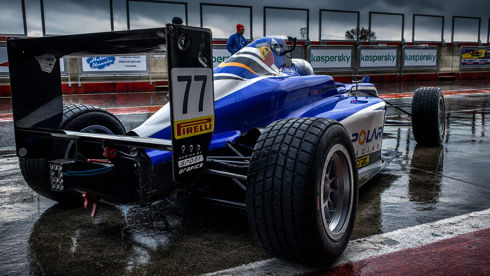 Blue Formula 4 car in a wet pit lane from the rear